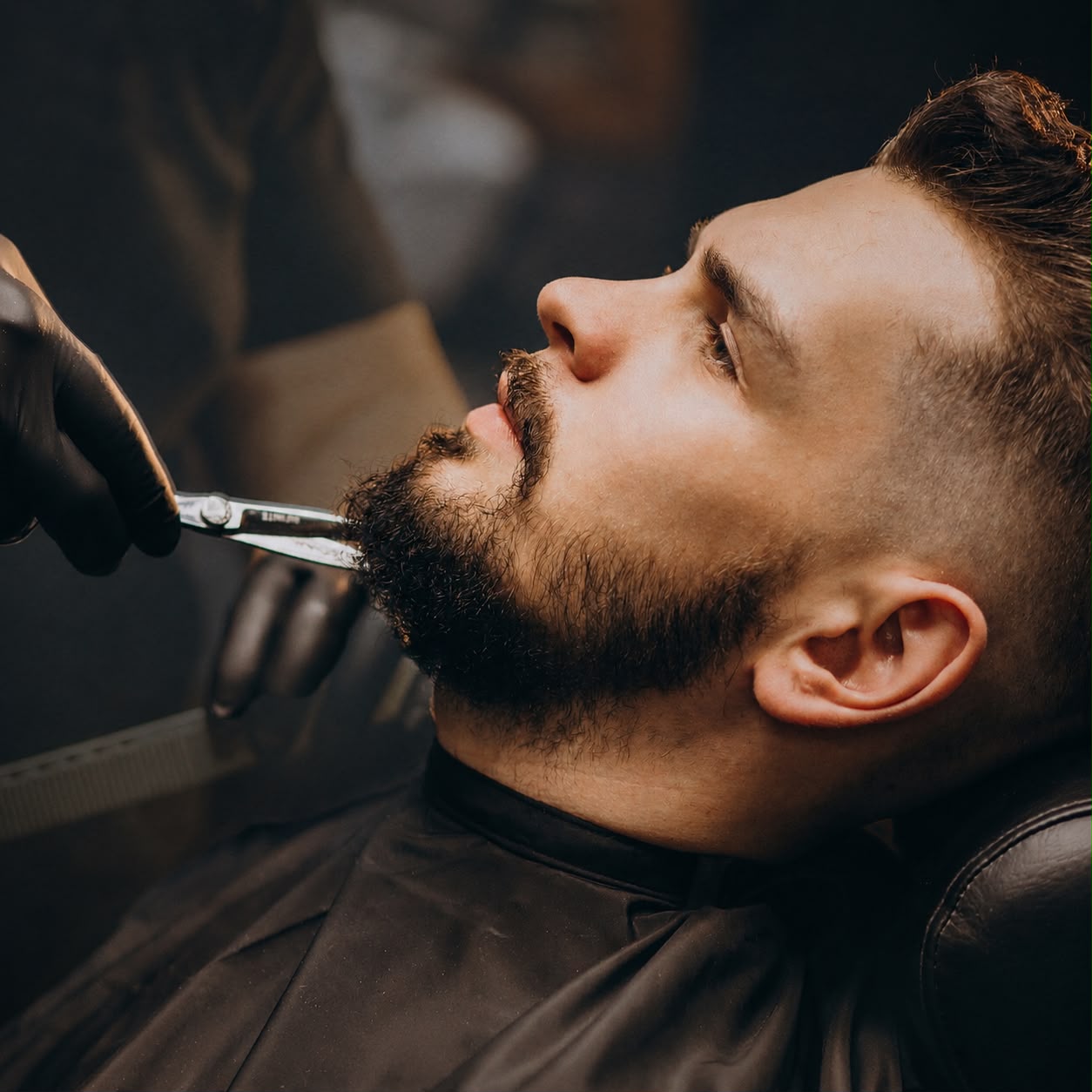 Barber trimming a client's beard with scissors
